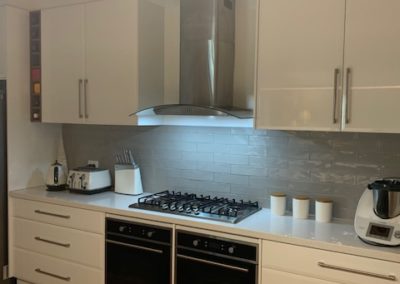 refurbished white kitchen, glossy white cupboard doors, double oven, long, shallow and medium depth draws, grey tiles that imitate the texture and shape of bricks, as a splash back